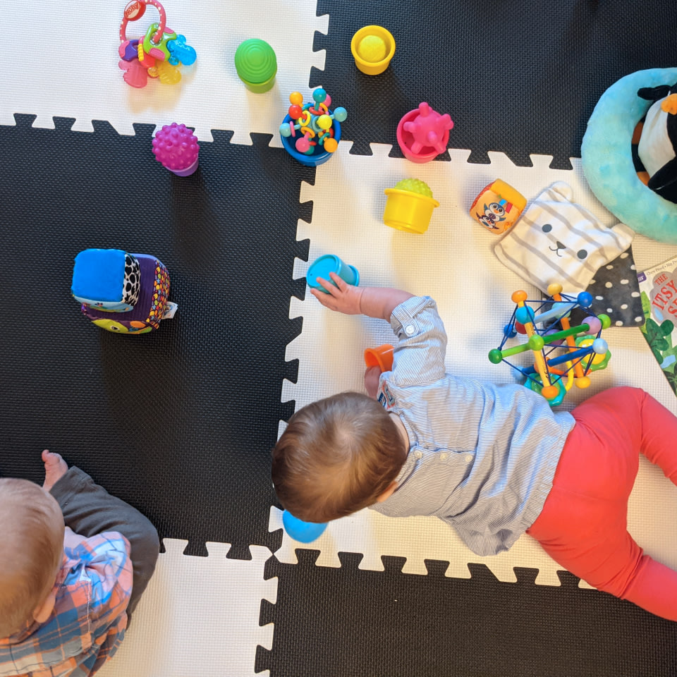 two toddlers playing with an assortment of toys on a black and white checkered puzzle mat