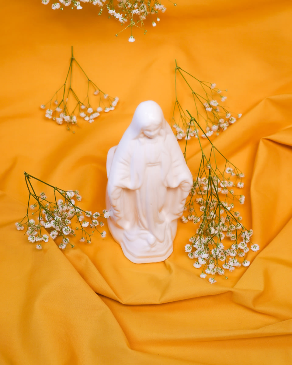 a photo of a porcelain Biblical figure surrounded by flowers on a yellow fabric spread