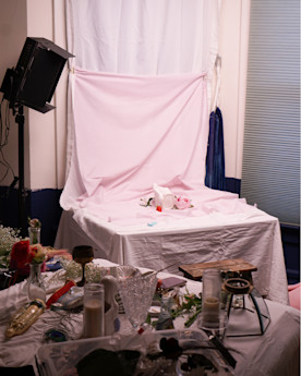 A photoshoot setup with assorted objects in the foreground: candles, glasses, flowers and more