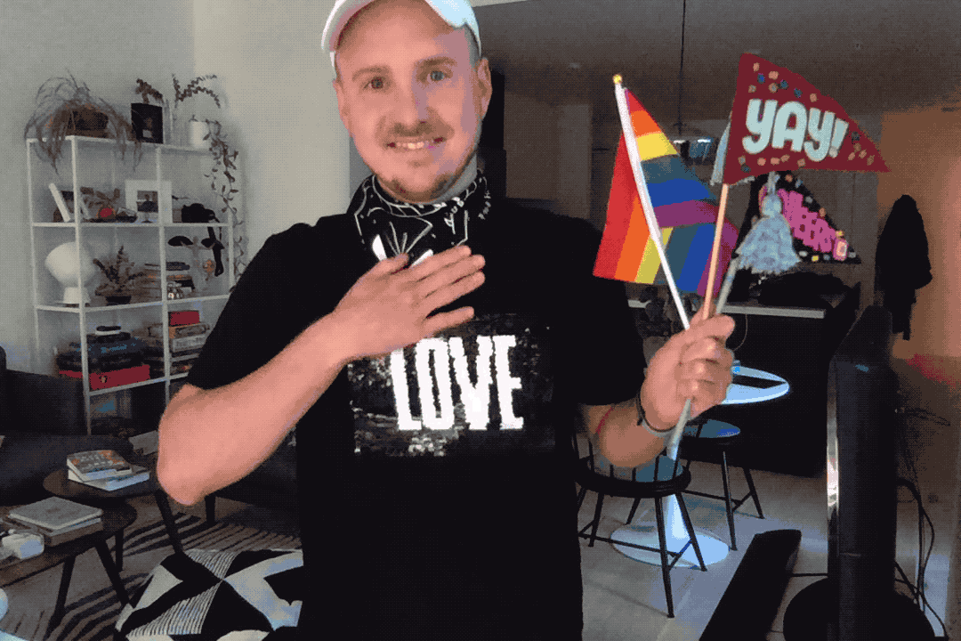 A gif of a squeers member wearing the bandana and a black t-shirt with a rainbow and holding a few celebratory flags
