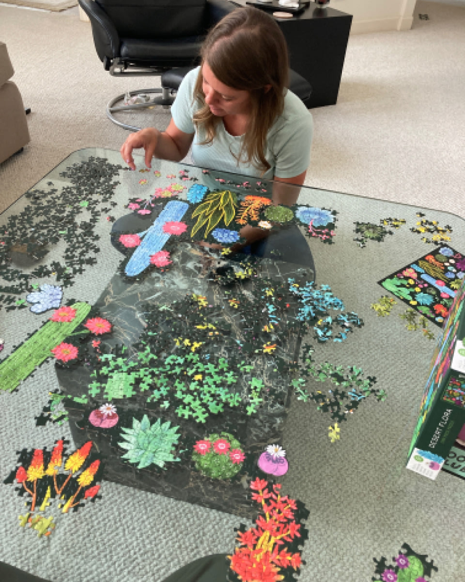a person sitting cross legged at a glass table working on a large puzzle