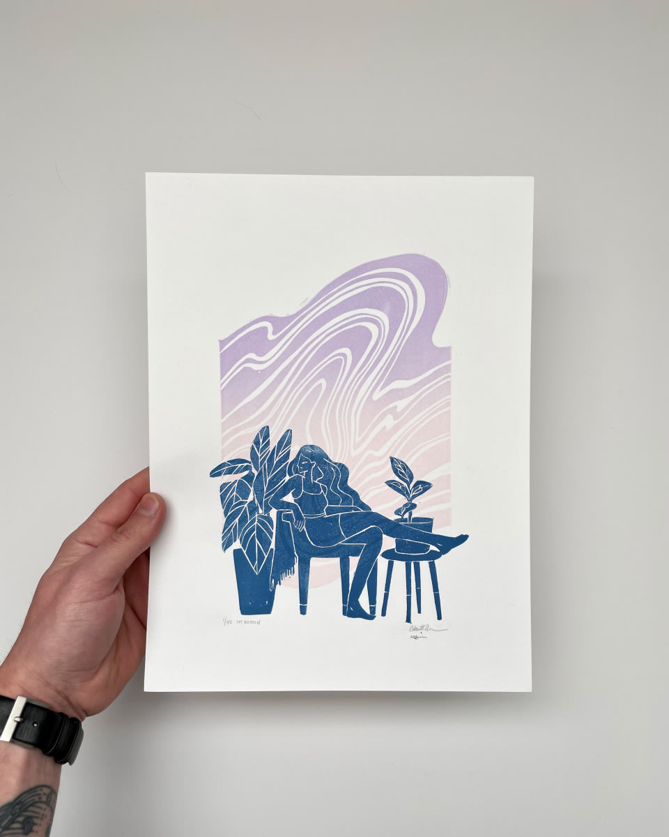 a hand holds a print with blue and lilac tones against a white wall