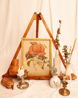 a photo of assorted objects arranged in a stylized composition, including an easel, lit candles, vases, and wicker objects