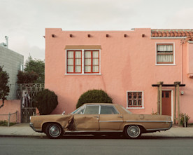 a photo of an antique car with visible damage parked in front of a coral colored house