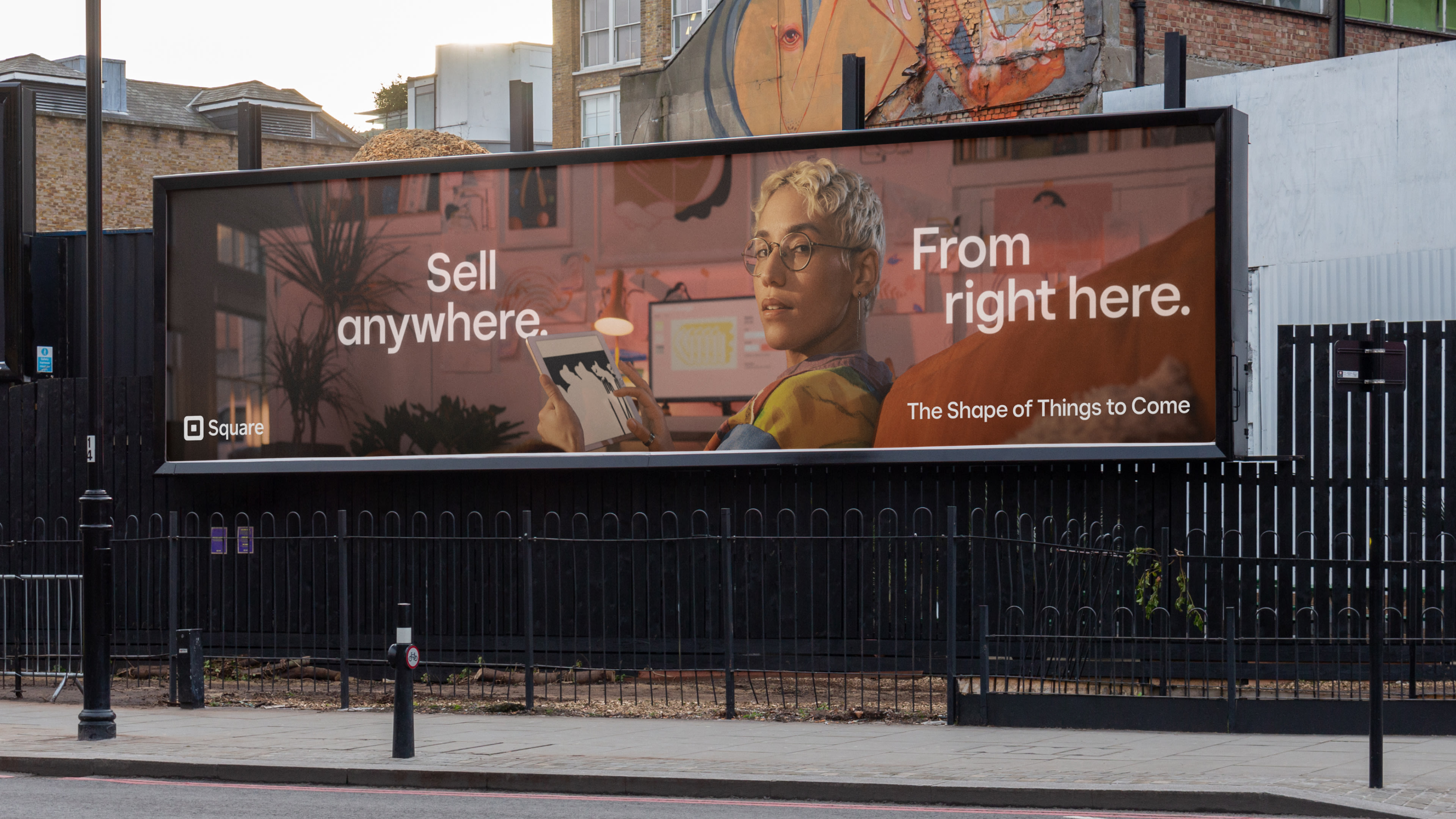 a photo of a billboard featuring a square ad with a person holding a tablet and the phrase: “Sell anywhere. From right here.”