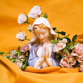 a photo of a porcelain Biblical figure surrounded by flowers on a yellow fabric spread