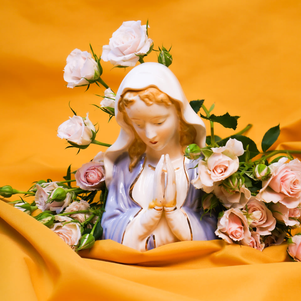 a photo of a porcelain Biblical figure surrounded by flowers on a yellow fabric spread