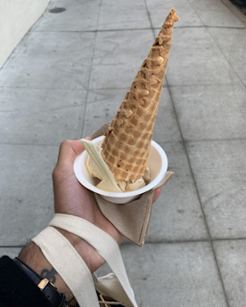 a hand holding an ice cream cone turned upside down into a small bowl