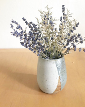 a textured vase on a wooden tabletop holding lavender