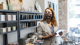 A shop owner wearing a mask uses a tablet to review inventory.