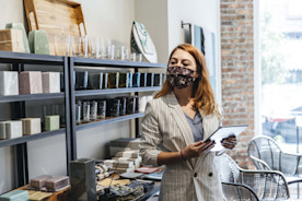 A shop owner wearing a mask uses a tablet to review inventory.
