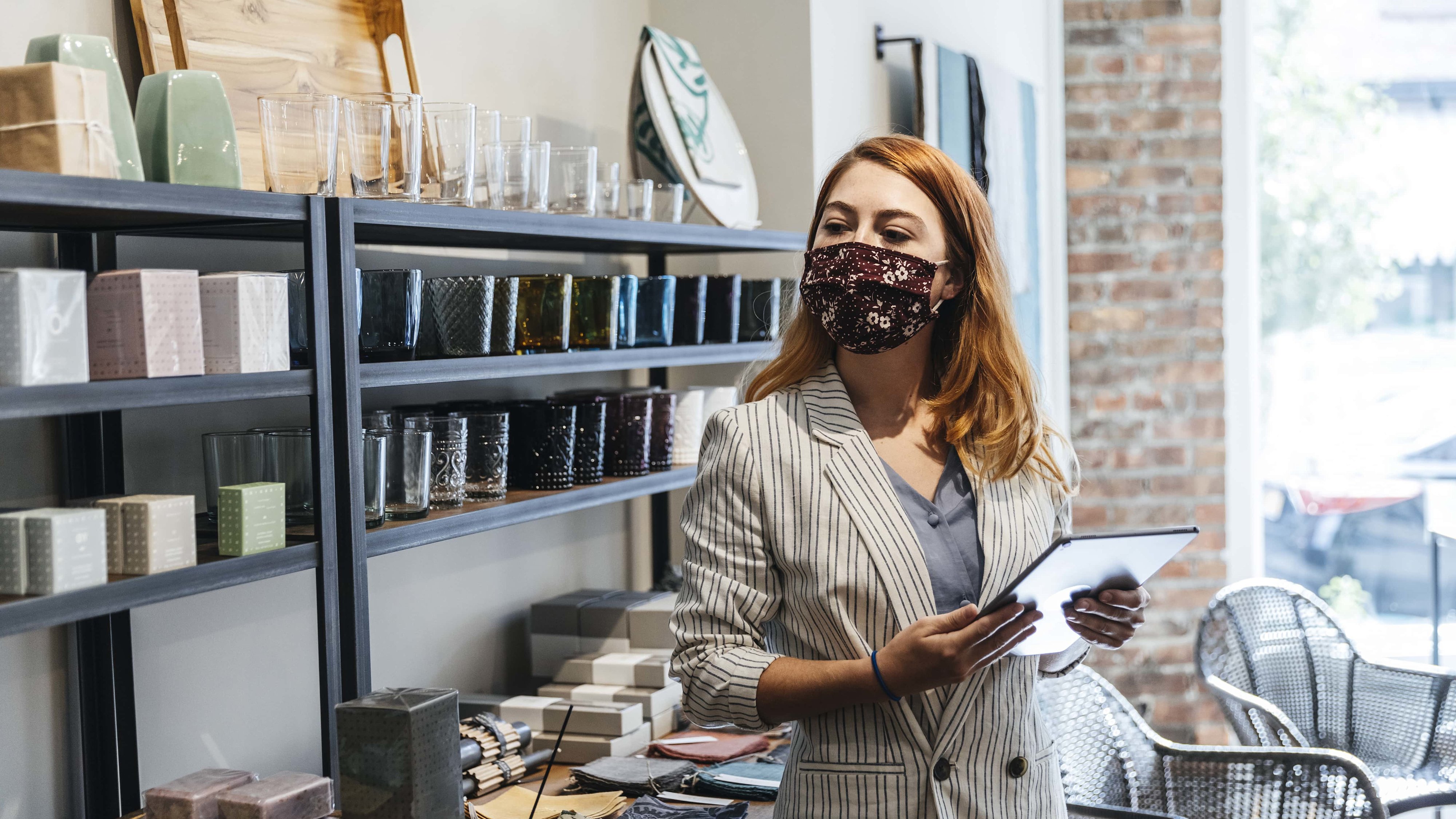 A shop owner wearing a mask uses a tablet to review inventory.