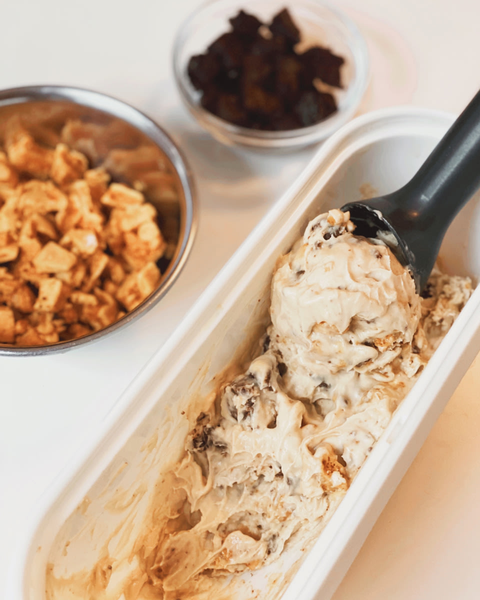 ice cream in a white oblong dish with a black scoop and with toppings in the background