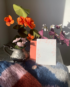 A card that reads “Happy Birthday” in an arrangement with flowers and a colorful throw blanket