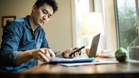 A business owner reviews paperwork at their desk with a laptop and smartphone.