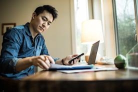 A business owner reviews paperwork at their desk with a laptop and smartphone.