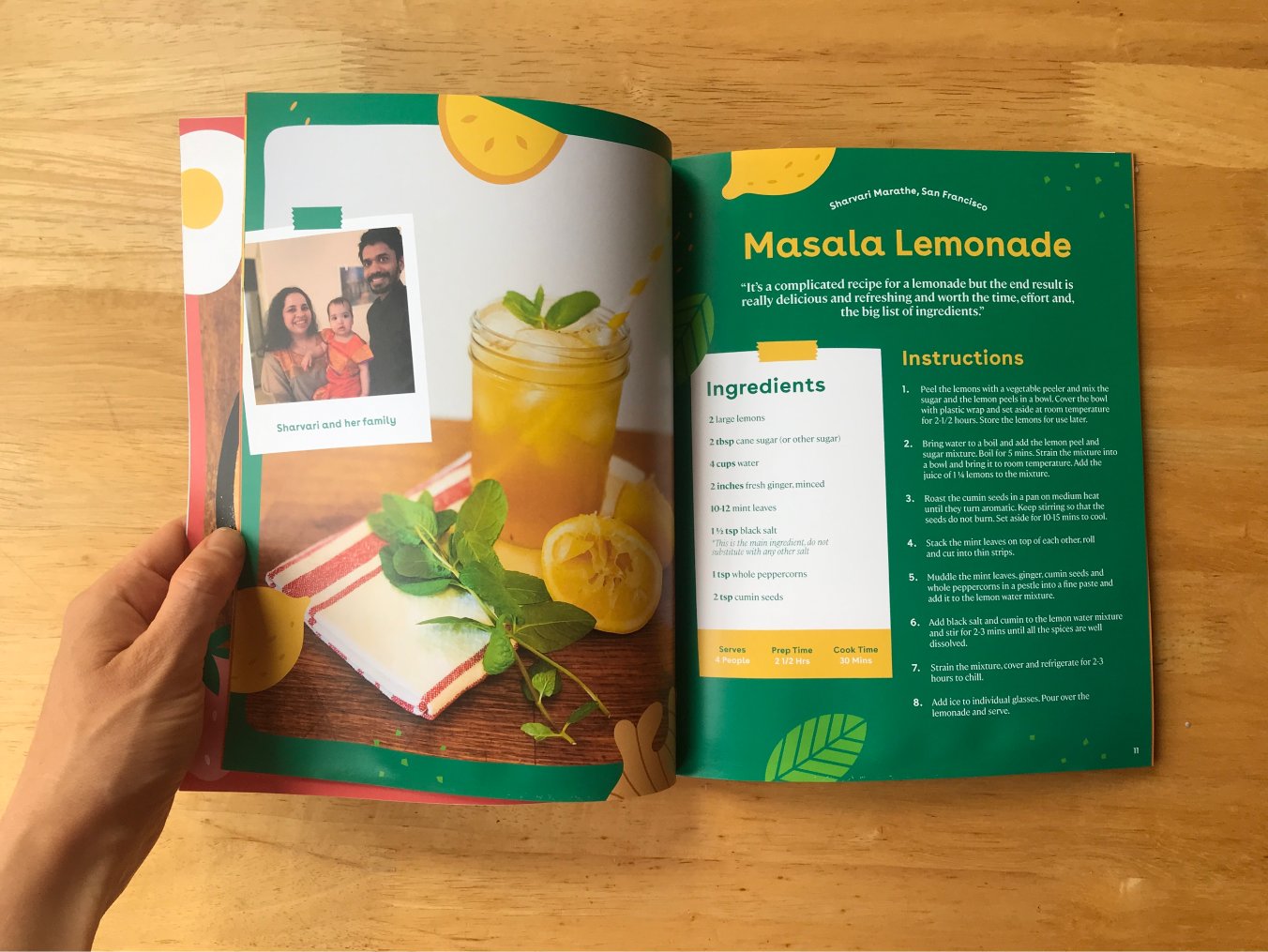 A spread of the cookbook outlining how to make Masala Lemonade held open by a hand all lying on a wooden surface