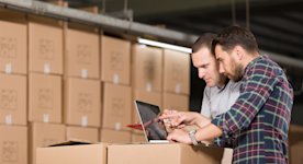 Two people looking at a laptop in a warehouse with boxes in the background