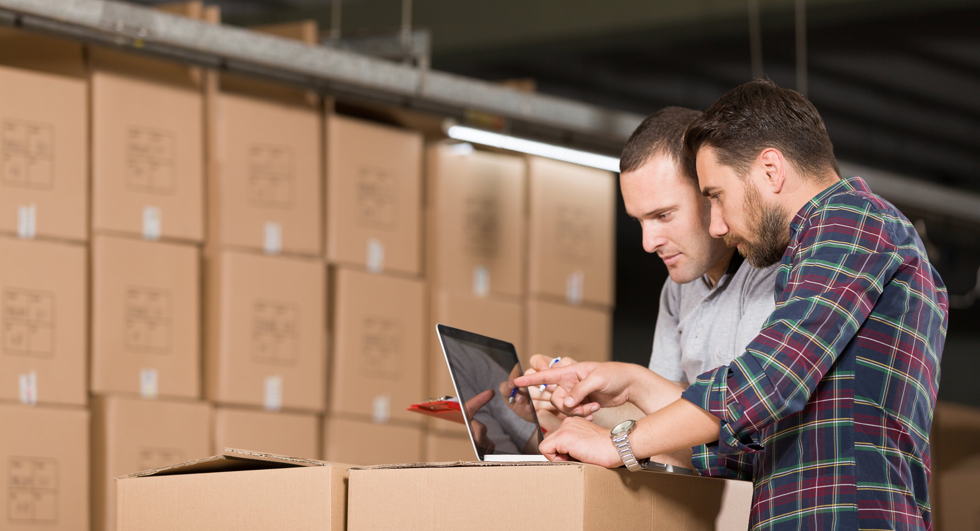 Two people looking at a laptop in a warehouse with boxes in the background