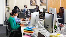 photo of people working at a shared desk space with large monitors