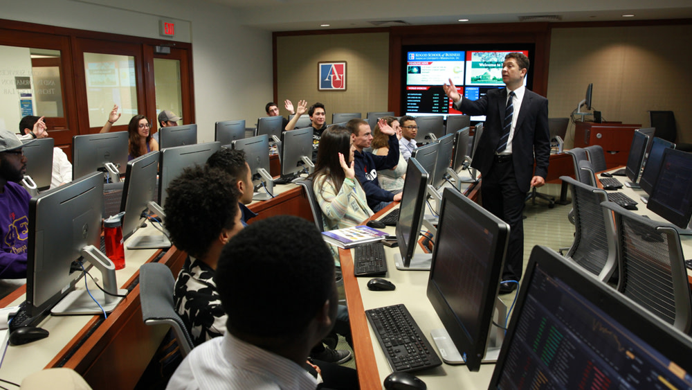 A class of data science students sit behind monitors and listen to their professor during a lecture at American University