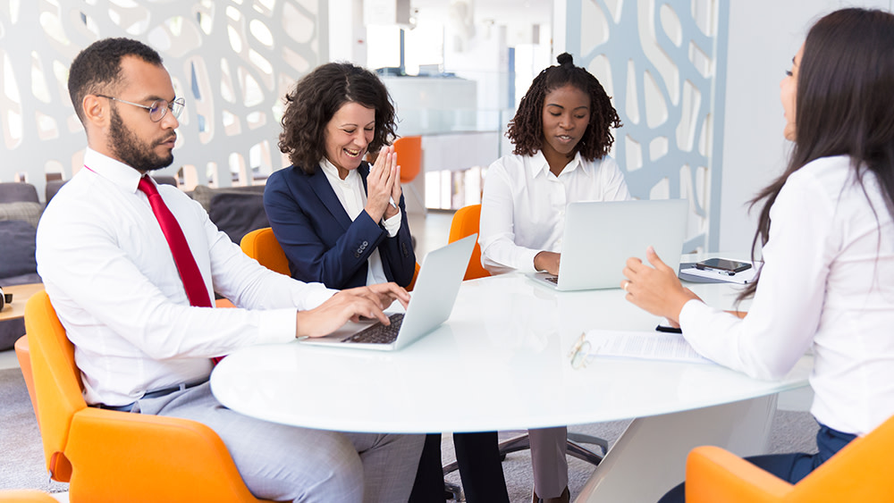 Four international students in business attire sit around a conference table in a modern office while working at an internship