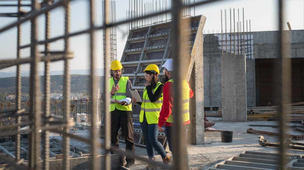 Two international students wearing hard hats and reflective vests stand on a construction site