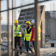 Two international students wearing hard hats and reflective vests stand on a construction site