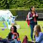 A group of international students at Heriot-Watt University in Edinburgh sit and stand on a lawn in front of a cow sculpture and have a conversation
