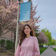 Gonzaga Global MBA student Daisy Le stands outside on campus in front of a flowering tree and green lawn and smiles for the camera