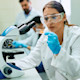 A female international student studying forensic science sits in front of a microscope at her US university laboratory and studies a glass slide.