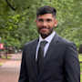 Mustafa, an international student from Saudi Arabia, stands in a suit and tie on the University of South Carolina campus and smiles for the camera.