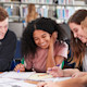 A group of international students sit together at a table in the university library and work together on an assignment.