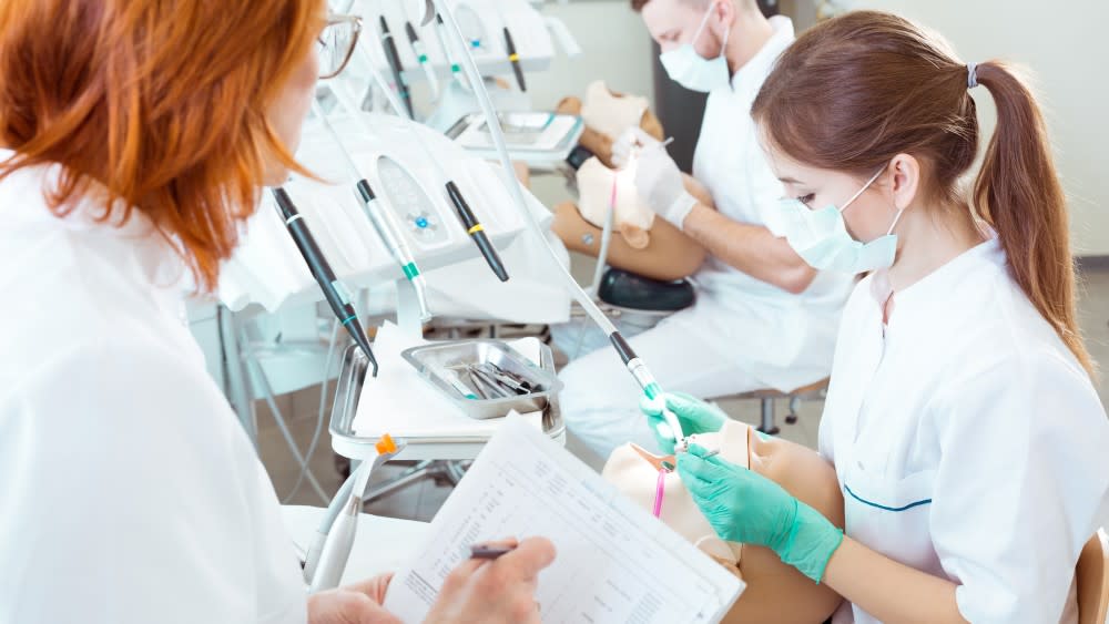In preparation for the DAT (also known as the DAT exam or DAT test), two dental students practice on mannequin replica patients at their university dental lab.