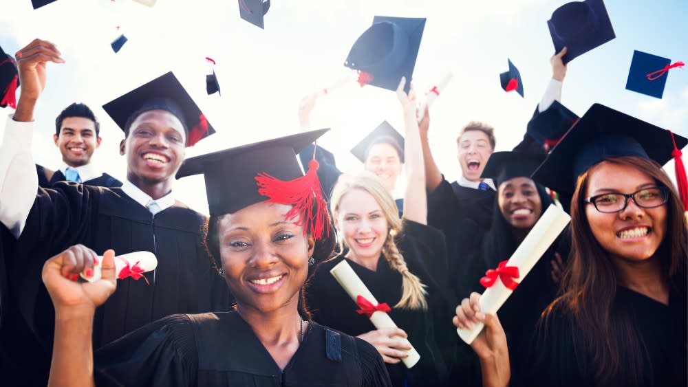 A group of smiling graduates in caps and gowns holding their diplomas