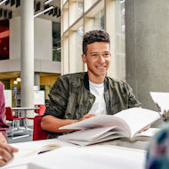 A male international student sits at a table in front of an open textbook