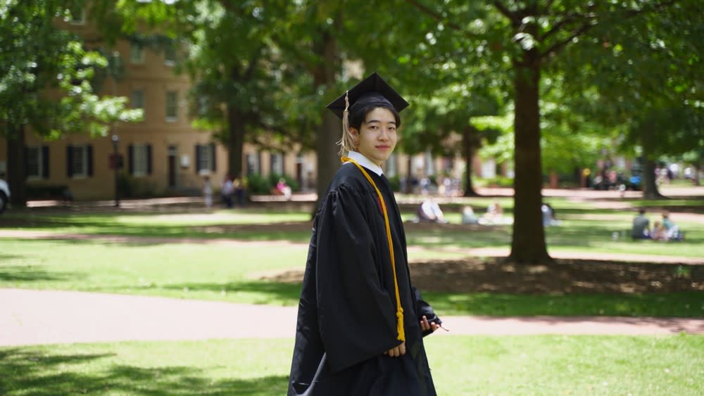 Chongbo, an economics student from China at the University of South Carolina, walks across campus in his graduation cap and gown