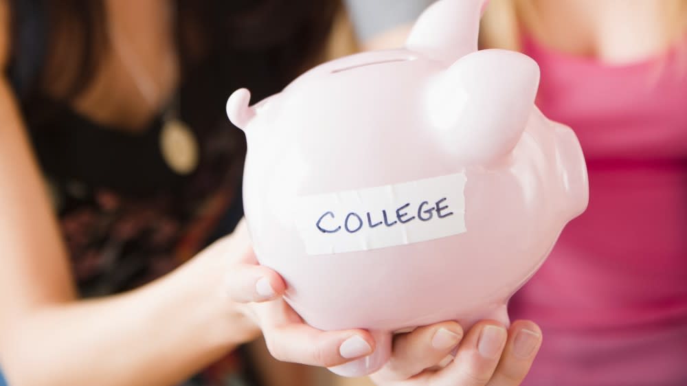 Two female international students hold out a piggy bank with the word COLLEGE taped on it