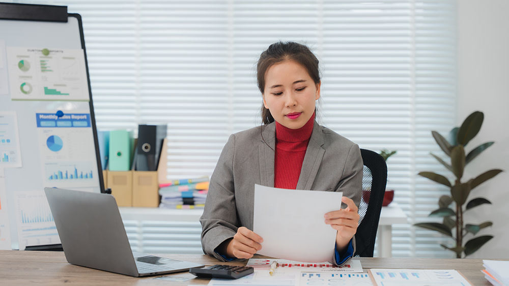 An Asian female student studying for a degree in business administration at her US university sits at a desk and studies a report.