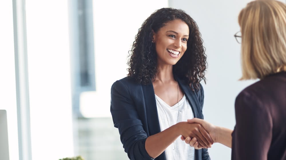 A woman with her back to the camera shakes hands with a woman after her interview. Practicing internship interview questions in advance gave her confidence during the meeting.