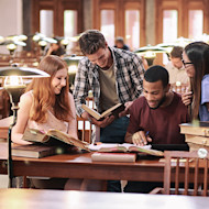 A group of four international students, two women and two men, sit at their US university library and study together.