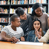 A group of international students earning their degrees in business administration sit at a table at their university library while working on a course project.