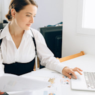 A female international student sits at a desk at home and uses a laptop while working on an assignment for her corporate finance class