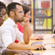Three international students sit in a row at a table of workstations in the library at their accredited US university.