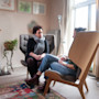 An international student sits on a wooden chair in a softly lit room across from a therapist on an ergonomic armchair during a mental health talk therapy session