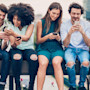 Five students sitting on a railing using English apps on their smartphones to practice their English language skills.