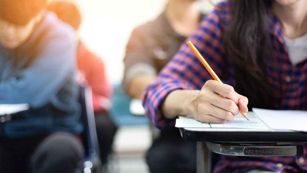 This photo shows a close-up of a student's hand holding a pencil while they take the IGCSE test as part of their study abroad university admissions process.
