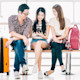 Three international students from Asia, each on an M-1 visa, sit on a bench at the airport with their luggage and wait for their flight to head to a US university campus.