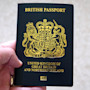 A hand holds a British passport for the United Kingdom of Great Britain and Northern Ireland