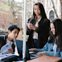 Three international students gather around a table on their US university quad and study together with books, a laptop, and a smartphone